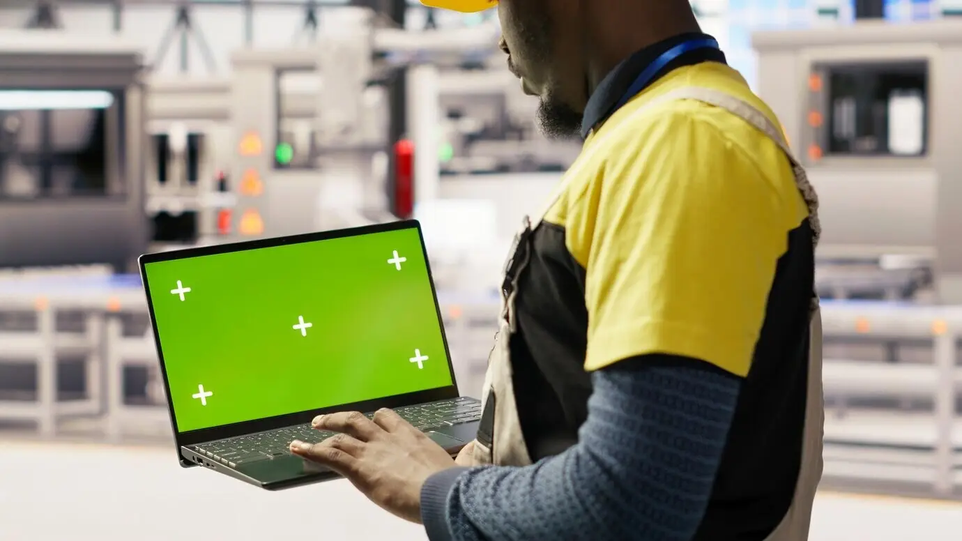 Ein Ingenieur in einer Fabrik für Solarpaneele analysiert Leistungsdaten mit einem Laptop mit grünem Bildschirm.